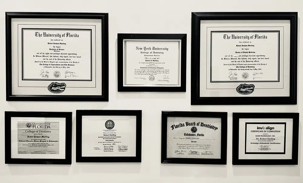 Framed dental certificates and diplomas displayed on white wall, showing professional qualifications.