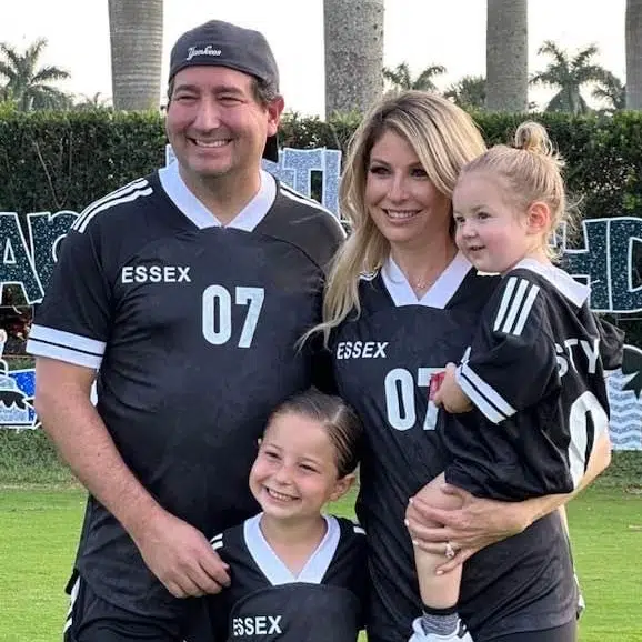 Family of four wearing matching Essex soccer jerseys posing together on field.