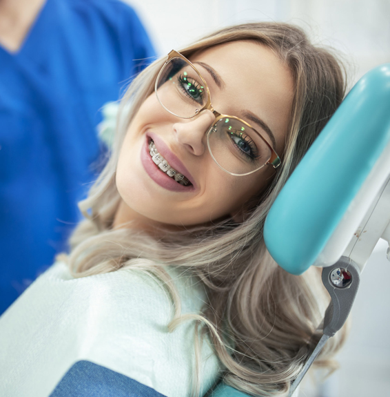 Young woman smiling in dental chair wearing glasses during orthodontic appointment.