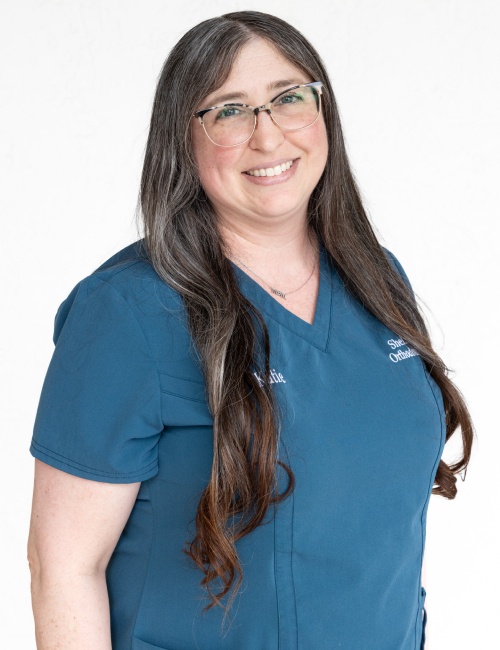 Female orthodontic professional wearing blue scrubs and glasses against white background.