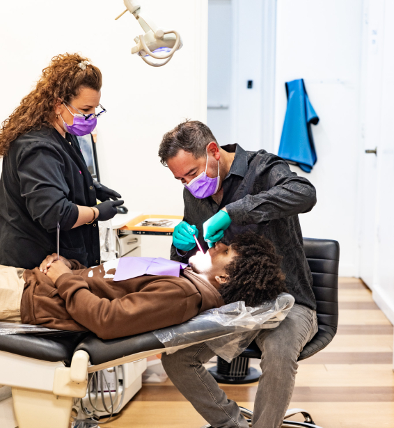 Two dental professionals examine a patient's teeth in a modern orthodontic clinic treatment room.