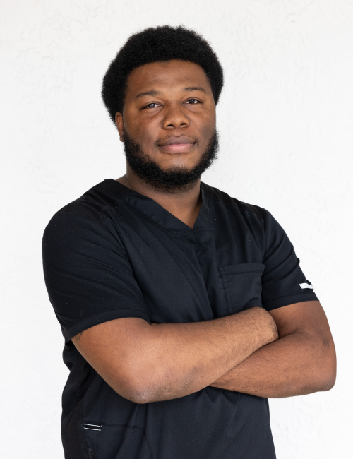 Professional male healthcare provider in dark scrubs with arms crossed against neutral background.