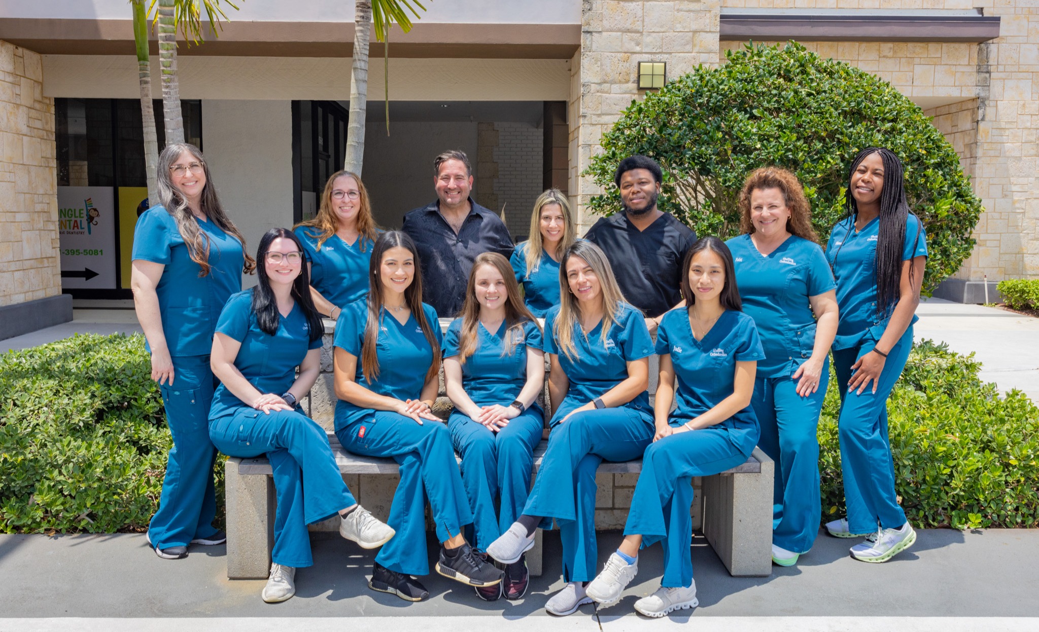 Orthodontics team in blue scrubs posed together outside modern dental office building.