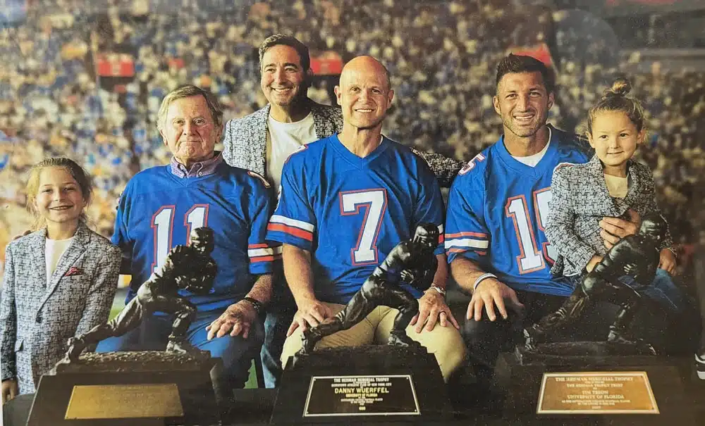 Florida Gators Heisman winners Spurrier, Wuerffel, and Tebow pose with their trophies at a Shelling Orthodontics event